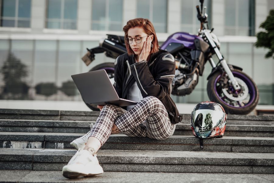 młoda dziewczyna z laptopem siedzi w pobliżu fioletowego motocykla
